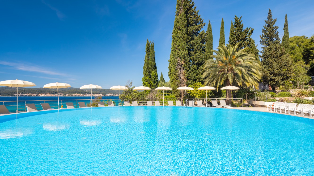 Outdoor pool at Orsan Maradiso Hotel by Aminess with white umbrellas and greenery.