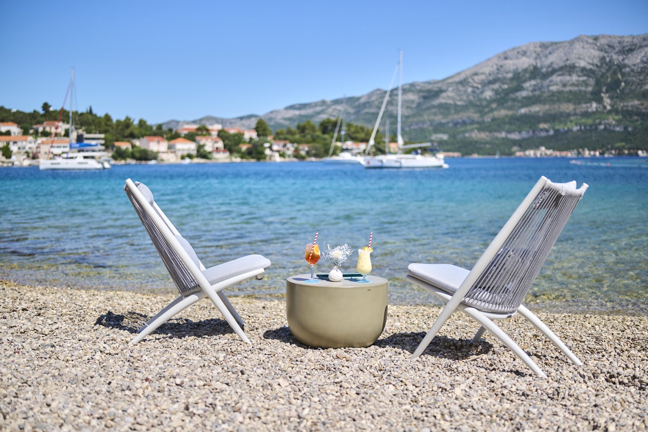 Eine entspannende Atmosphäre in der Puntomare Fun Beach Zone in der Nähe von Aminess Port9 Planet Camping Korcula, mit einem Strandtisch mit Getränken, Sonnenliegen und einem malerischen Küstenblick