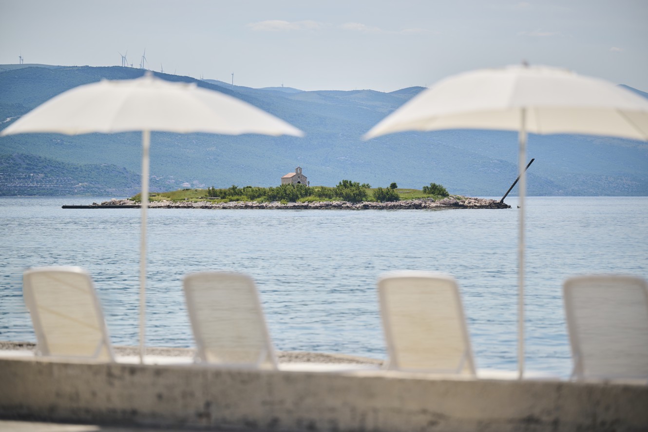 Ležalniki in senčniki ob morju s pogledom na otoček pred hotelom Aminess Lišanj.