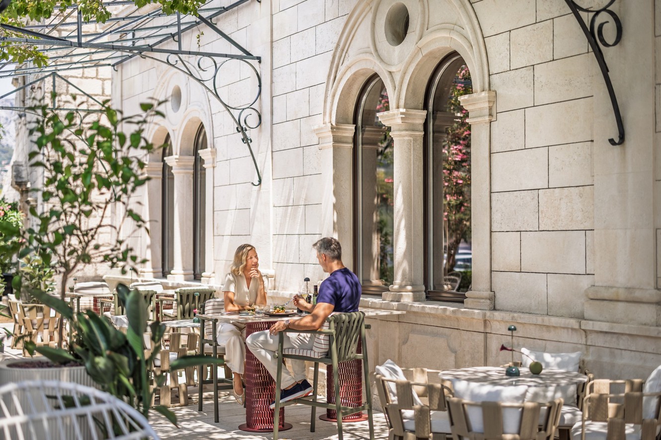 A couple dines on the terrace of Aminess Younique Korcula Heritage Hotel by the stone facade.