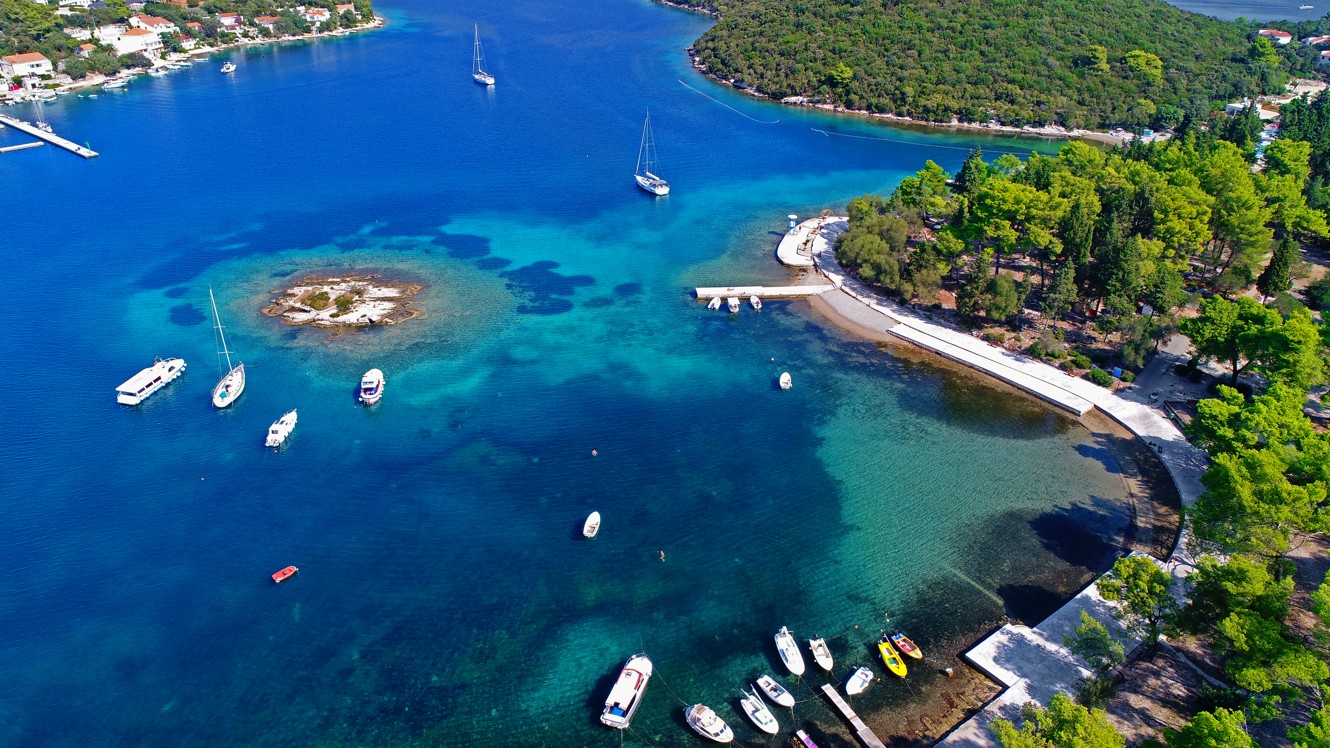 Eine atemberaubende Luftaufnahme der Bucht von Korcula in der Nähe von Aminess Port9 Planet Camping, zeigt lebhaft türkisfarbenes Wasser, kleine verankerte Boote und eine üppig grüne bewaldete Küste