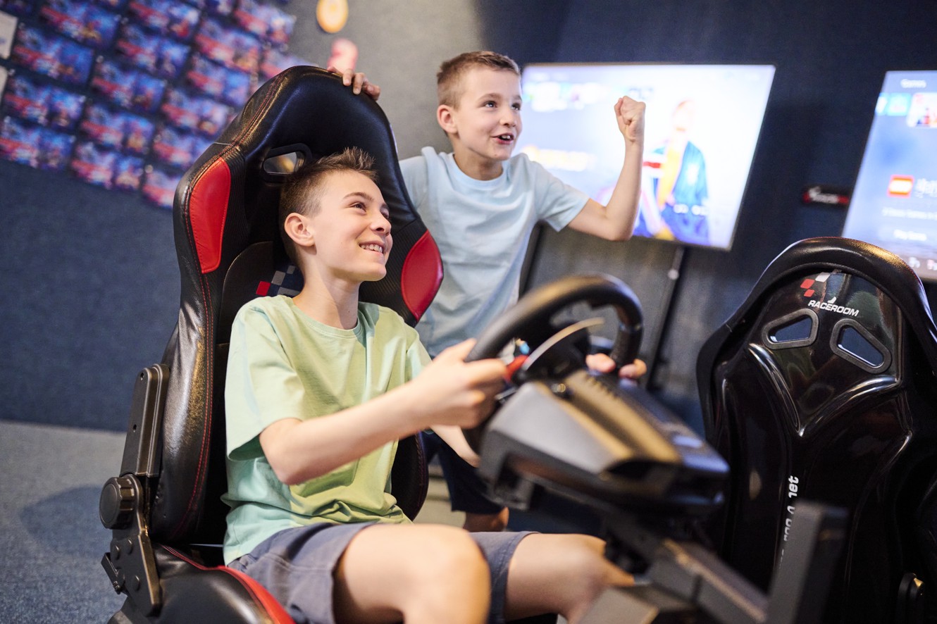 Boys play a racing video game in a gaming room with a driving simulator