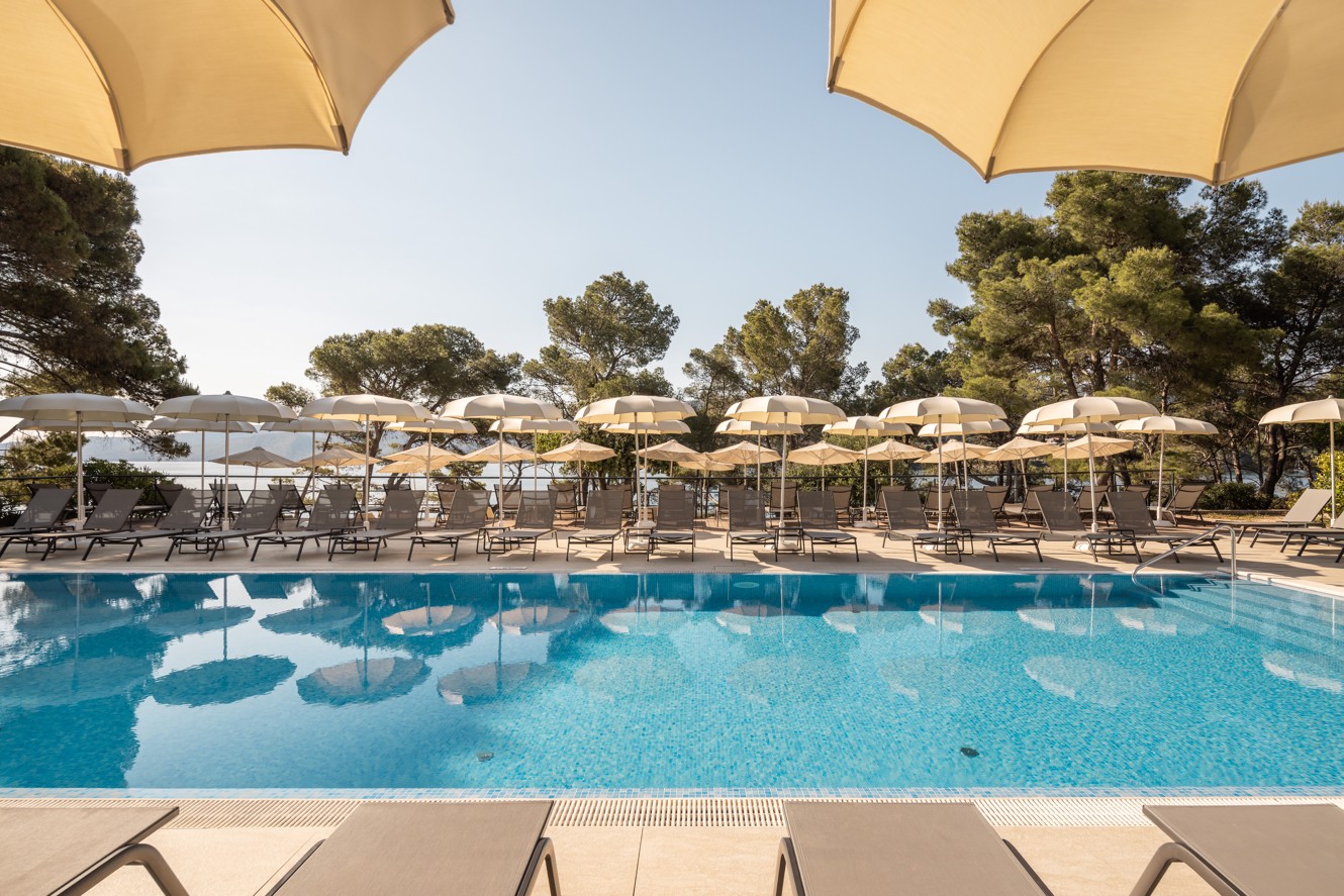 Outdoor pool with sun loungers and parasols surrounded by pine trees at Aminess Younique Senses Resort on Hvar island