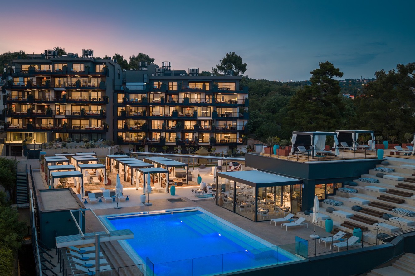 Younique Vollo Hotel Residences u sumrak s osvijetljenim bazenom i kabinama.