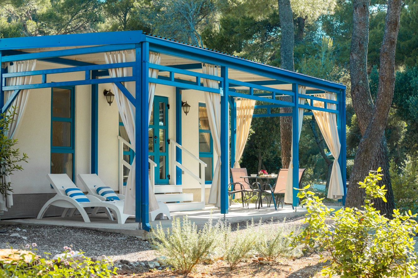 Terrazza con lettini prendisole e zona salotto davanti alla casa mobile presso Planet Camping Holiday Homes Port9 by Aminess, immersa nel verde mediterraneo.