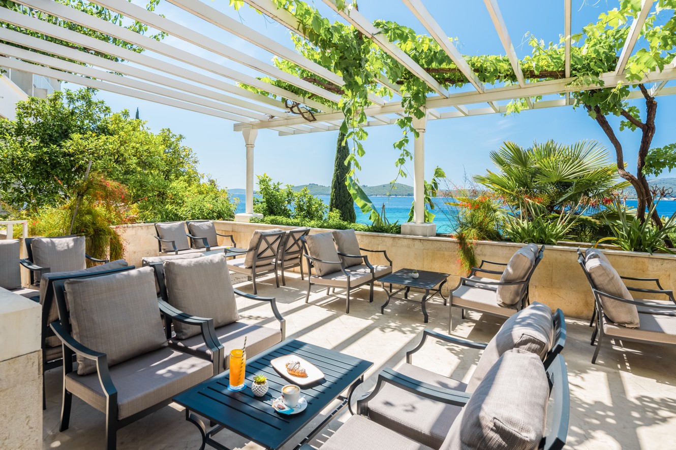 Een charmant terras bij Maradiso Orsan by Aminess Hotel in Orebic met een aperitiefbar met zitplaatsen onder weelderige wijnstokken, met uitzicht op de Adriatische Zee en het groen.