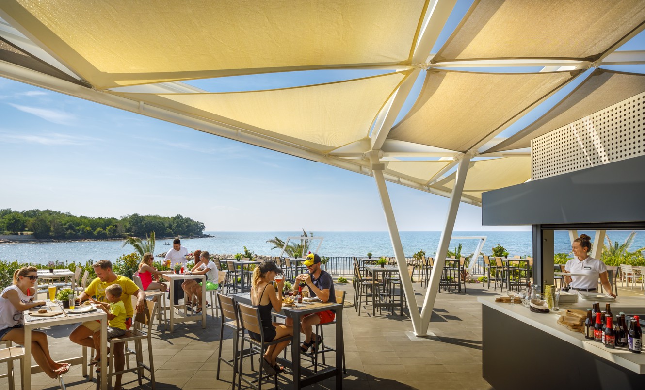 Gäste genießen ihre Mahlzeiten in einem Restaurant in der Nähe des Meeres im Aminess Planet Camping Maravea, Novigrad