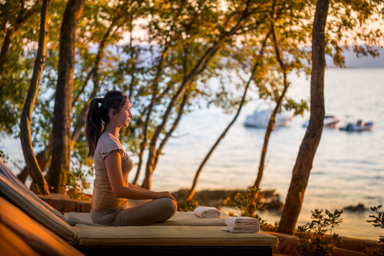 Gost uživa v mirni seansi joge, obdan z naravo, s pogledom na morje v počitniški hiši Aminess Style Camping Atea Resort.