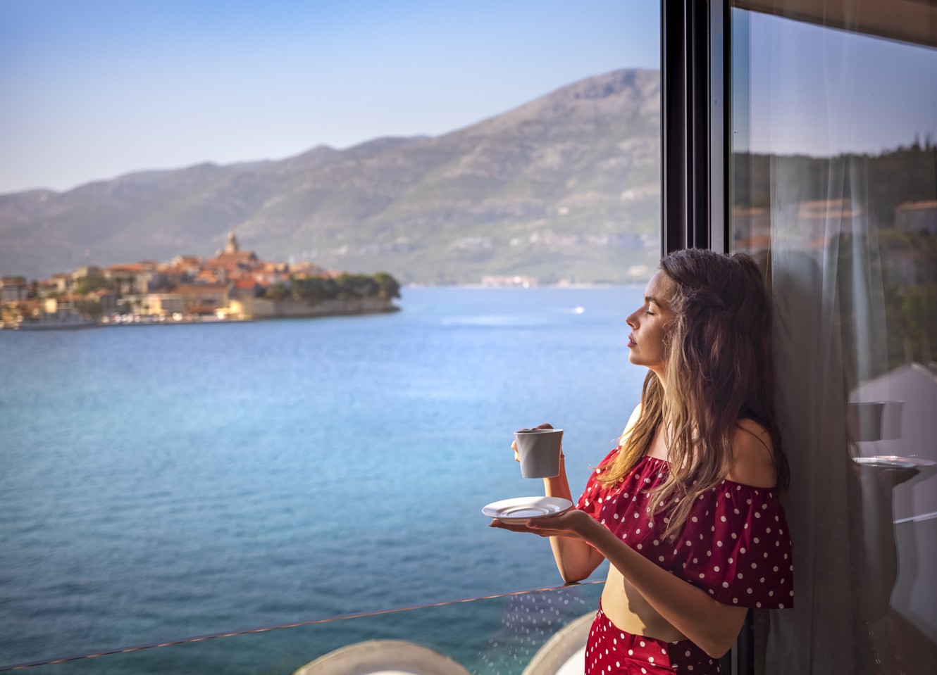 Dame entspannt am Fenster des Zimmers mit Blick auf die Altstadt von Korcula im Aminess Younique Liburna Hotel.