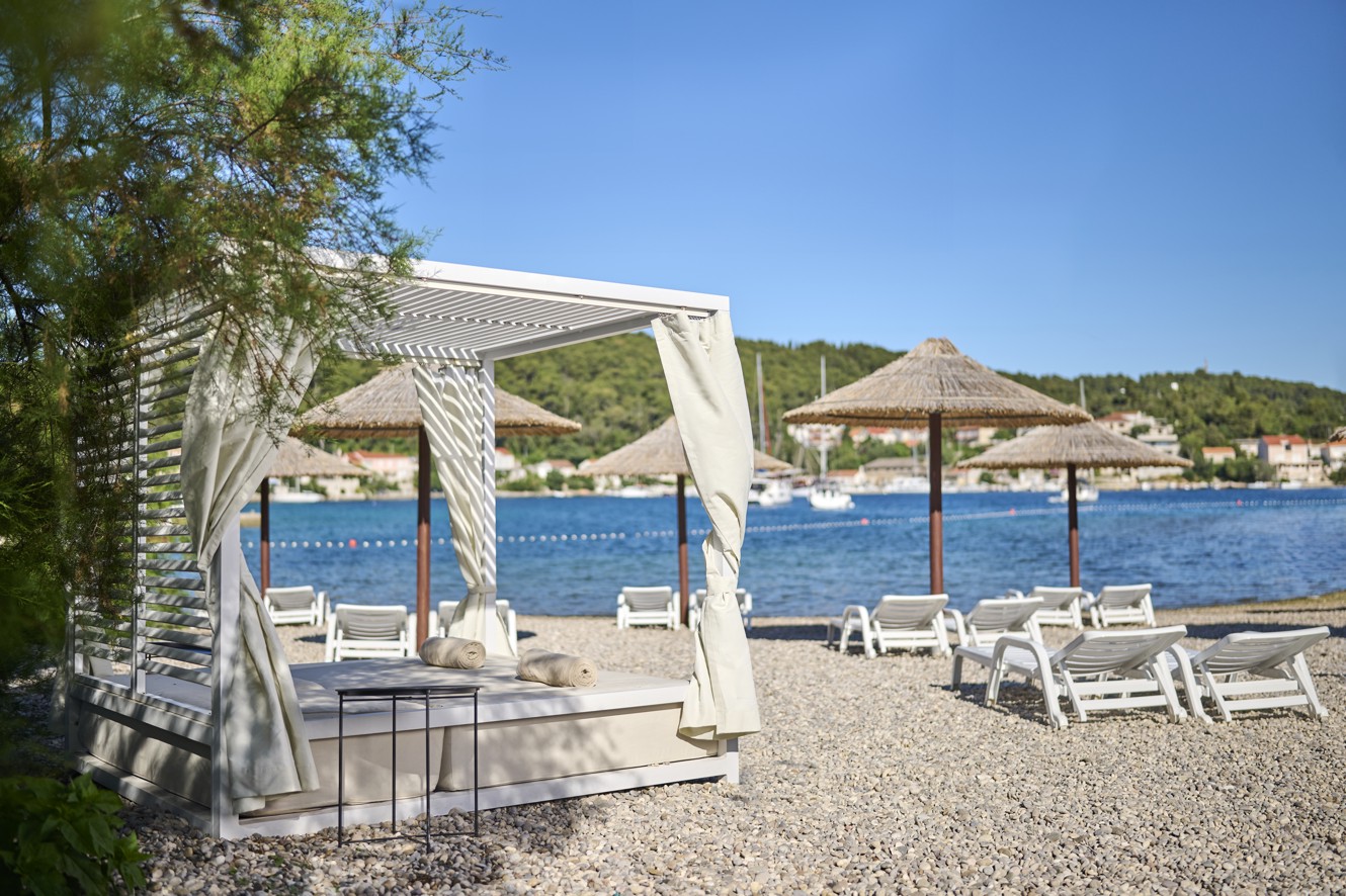 A canopy bed on the pebble beach, providing a comfortable spot to relax and enjoy the sea view at Aminess Vival Port9 Resort in Korcula.