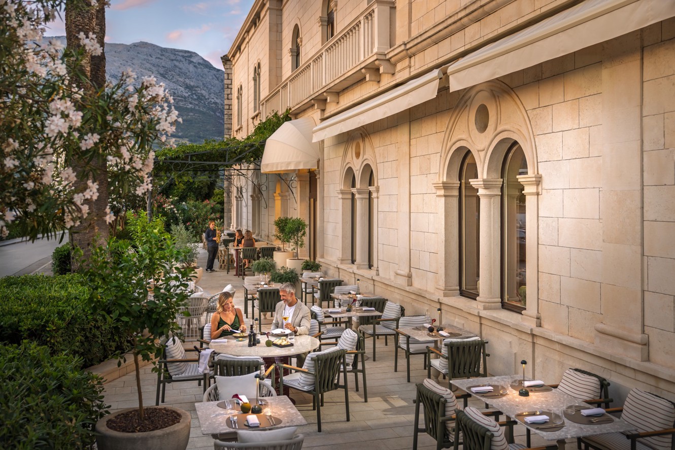 A couple dines on the terrace of Aminess Younique Korcula Heritage Hotel by the stone facade.
