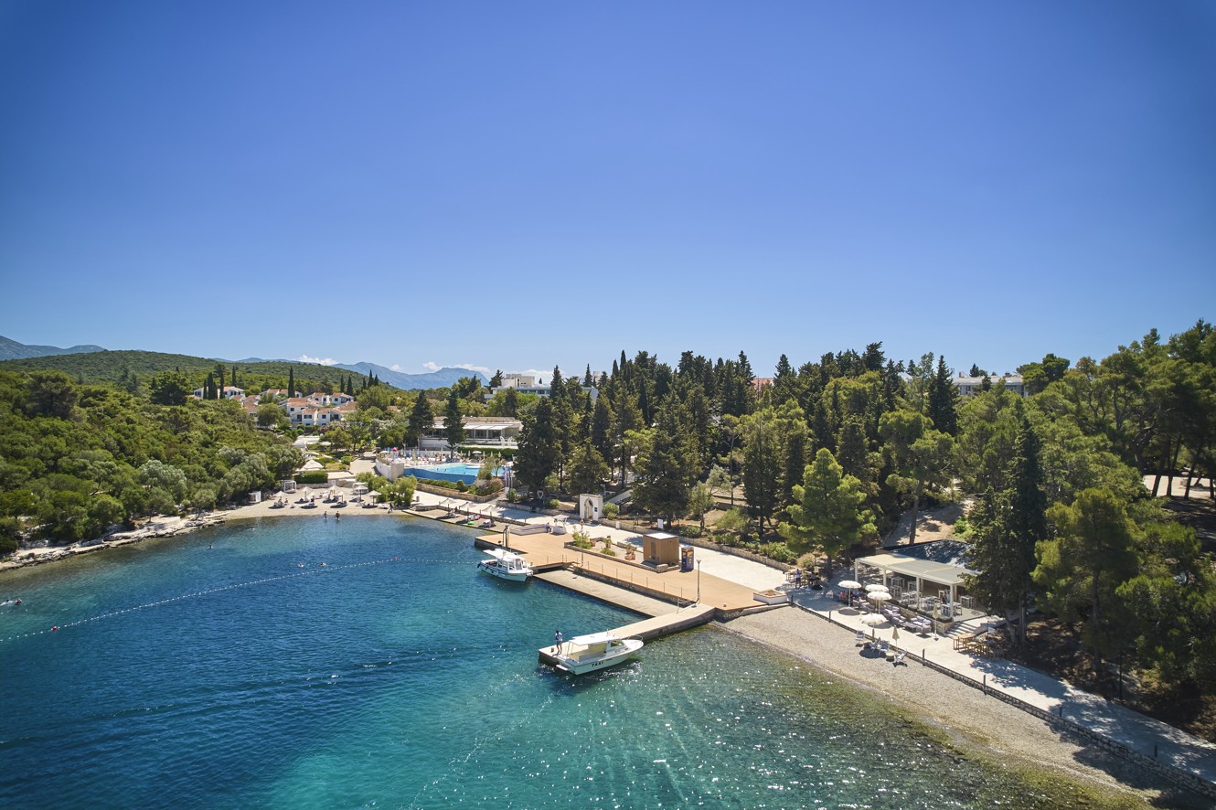 Ein Panoramablick auf die Bucht in der Nähe von Aminess Port9 Planet Camping Korcula, der das klare blaue Wasser, den mit Kiefern bewachsenen Ufer und einen Sandstrand hervorhebt, der ideal für Entspannung auf der Insel Korcula ist.