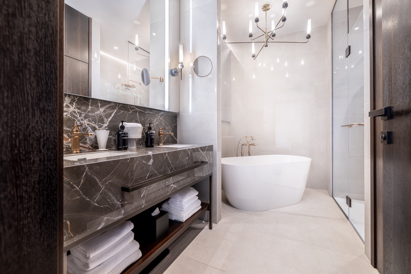 Modern hotel bathroom with a freestanding bathtub, marble vanity and glass shower.