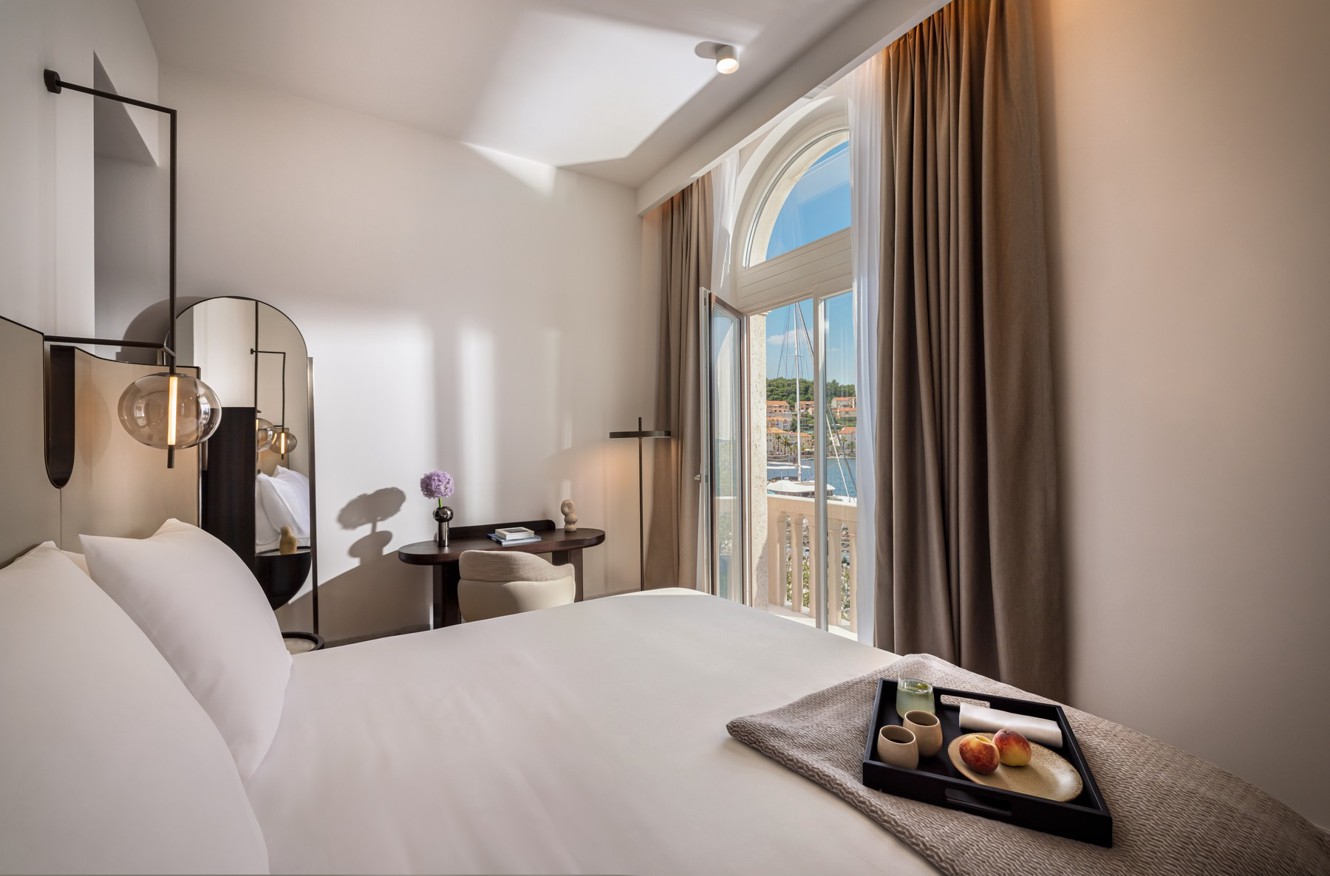 Modern Aminess hotel room with breakfast on the bed and a marina view.