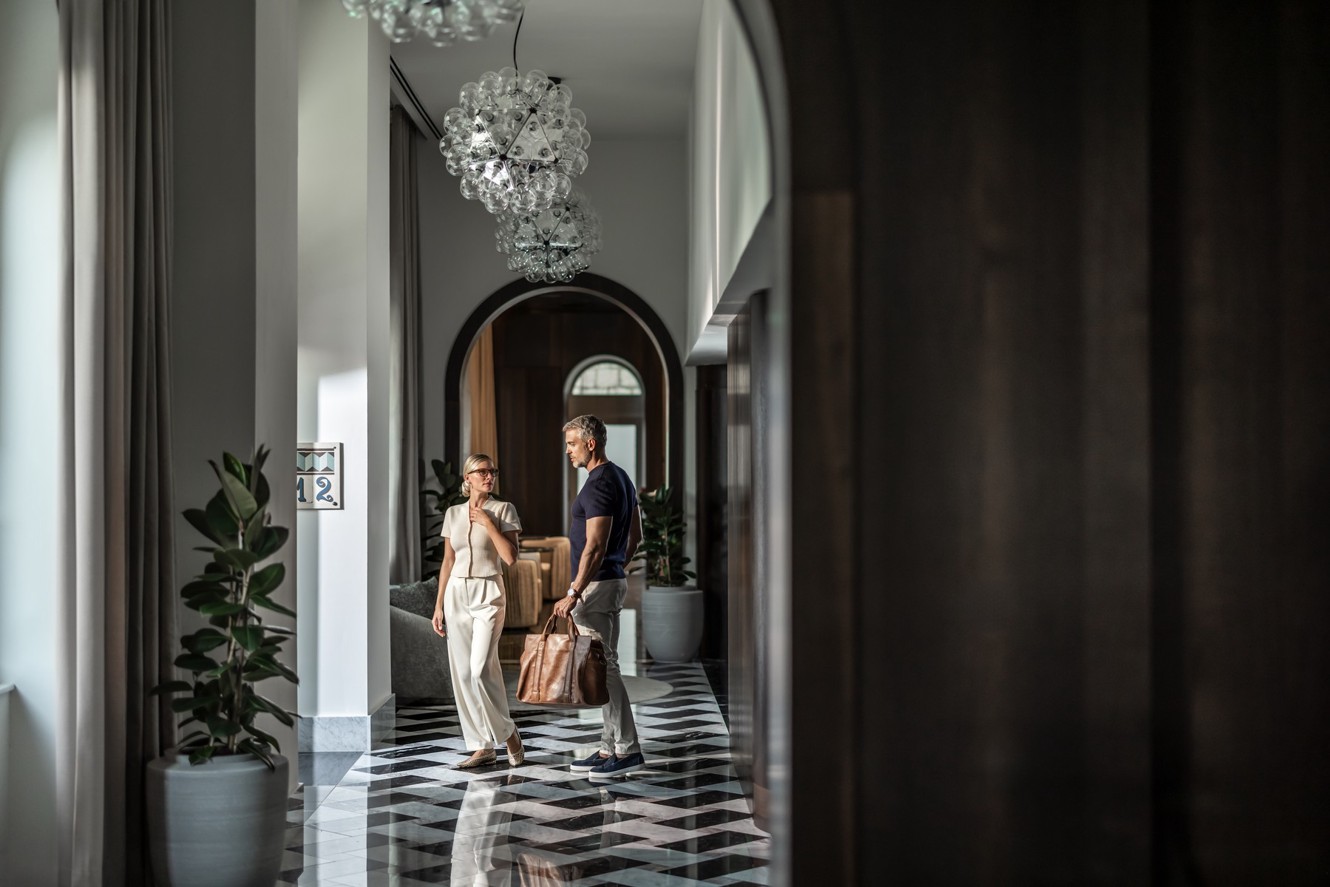 A couple with a travel bag talks in the corridor of Aminess Younique Korcula Heritage Hotel.