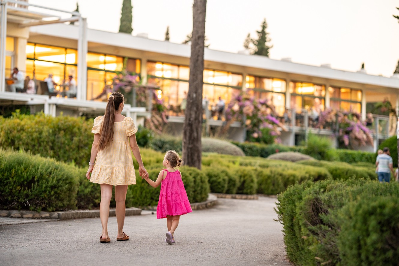 Mother holding her daughter by the hand a walking in the garden of the Aminess Vival Velaris Resort in Brač
