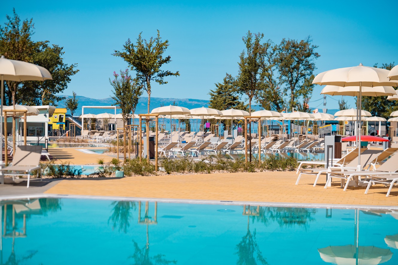 Sprostitveno območje bazena z ležalniki, senčniki in pogledom na morje v Aminess Style Camping Atea Resortu.