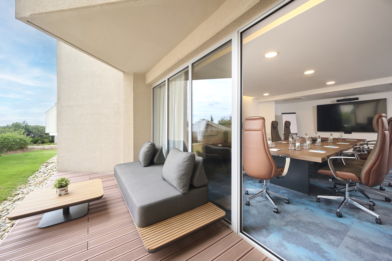 L'immagine mostra la sala conferenze Burin, allestita per un incontro, con una terrazza esterna dotata di un tavolo, divano e verde.