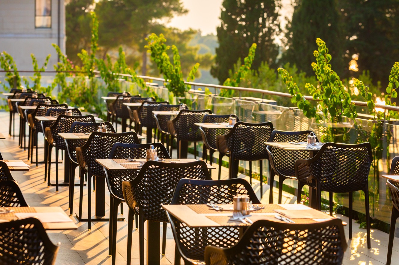 Outdoor terrace of Oliveto restaurant at Aminess Vival Velaris Resort, Brač, with modern black chairs and a view of greenery in golden sunset light
