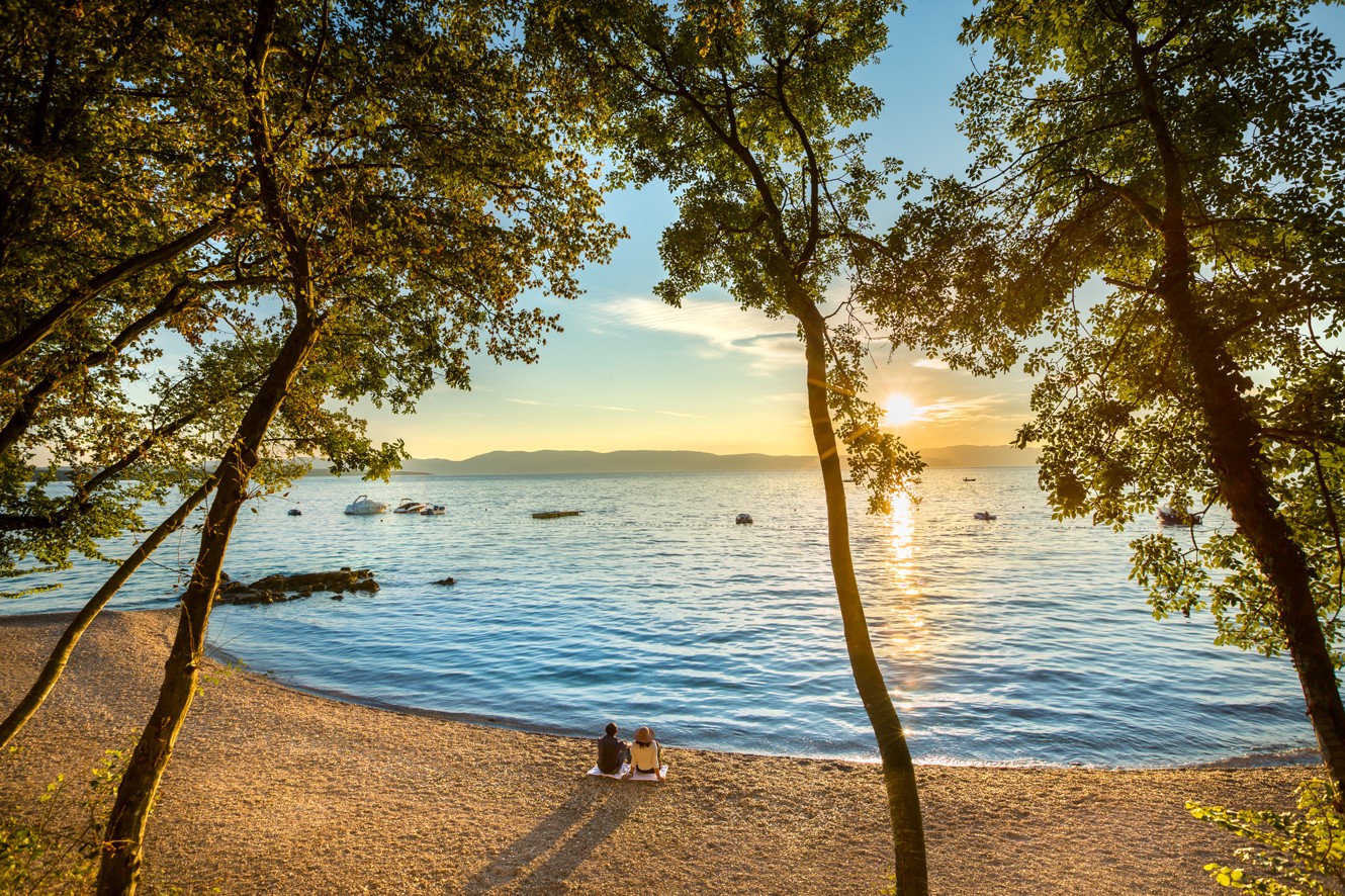 Mirni pogled na plažu okviren s drevesi, s pogledom na čisto Jadransko morje v Aminess Style Camping Atea Resort.