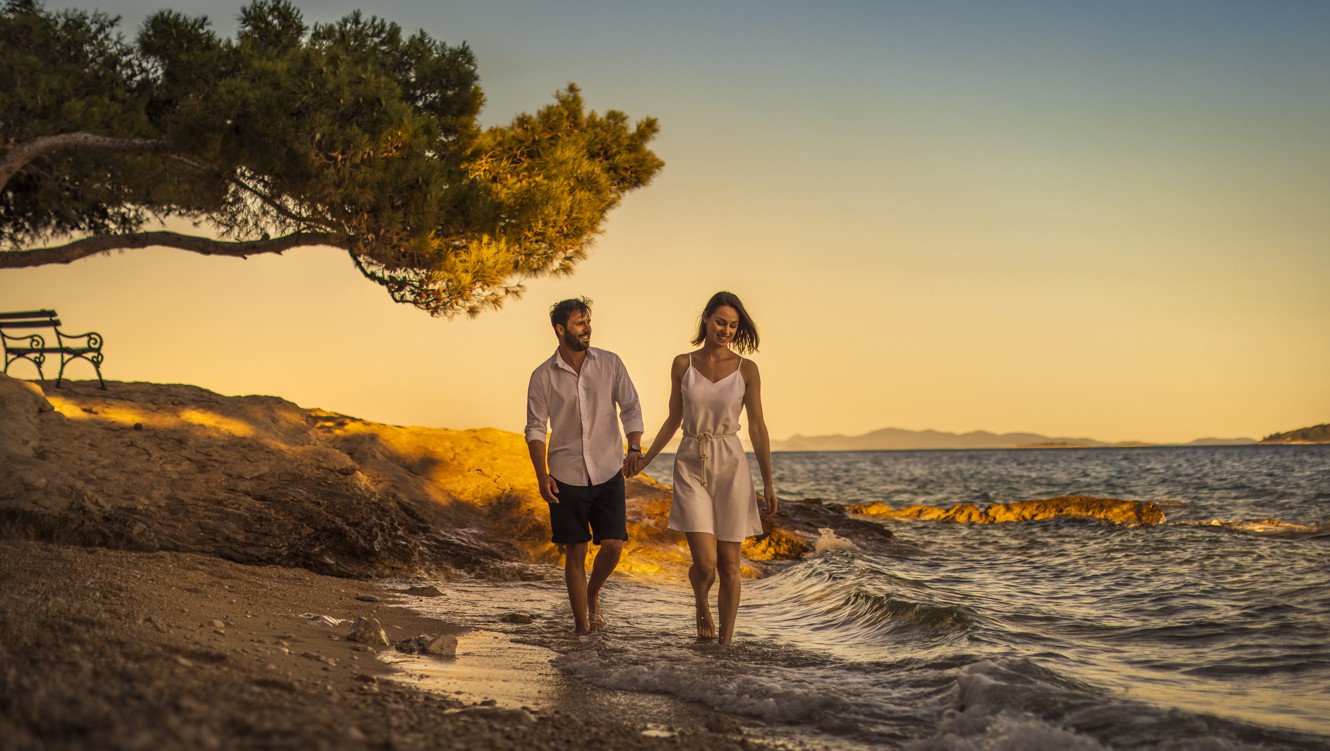 Ein romantisches Paar schlendert bei Sonnenuntergang am Strand in Orebic, Kroatien in der Nähe von Aminess Maradiso Bellevue Village.