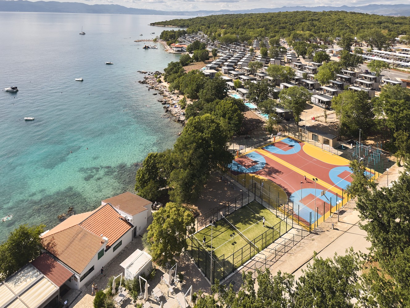 Pogled na novo živahno športno središče letovišča, ki se ponaša z igrišči, obdanimi z bujnim zelenjem, in mirno jadransko obalo v Aminess Style Camping Atea Resort.