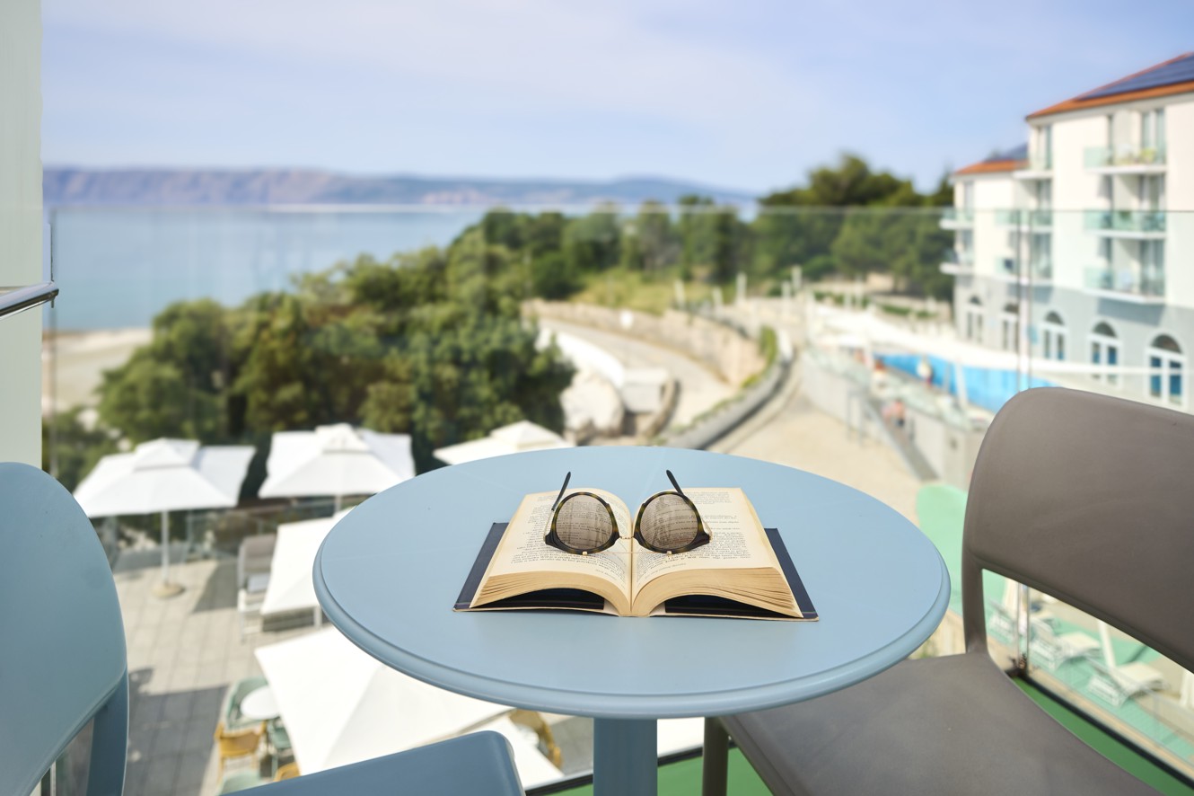 Pogled na morje z balkona hotela Aminess Lišanj Premium, s knjigo in sončnimi očali na mizi.