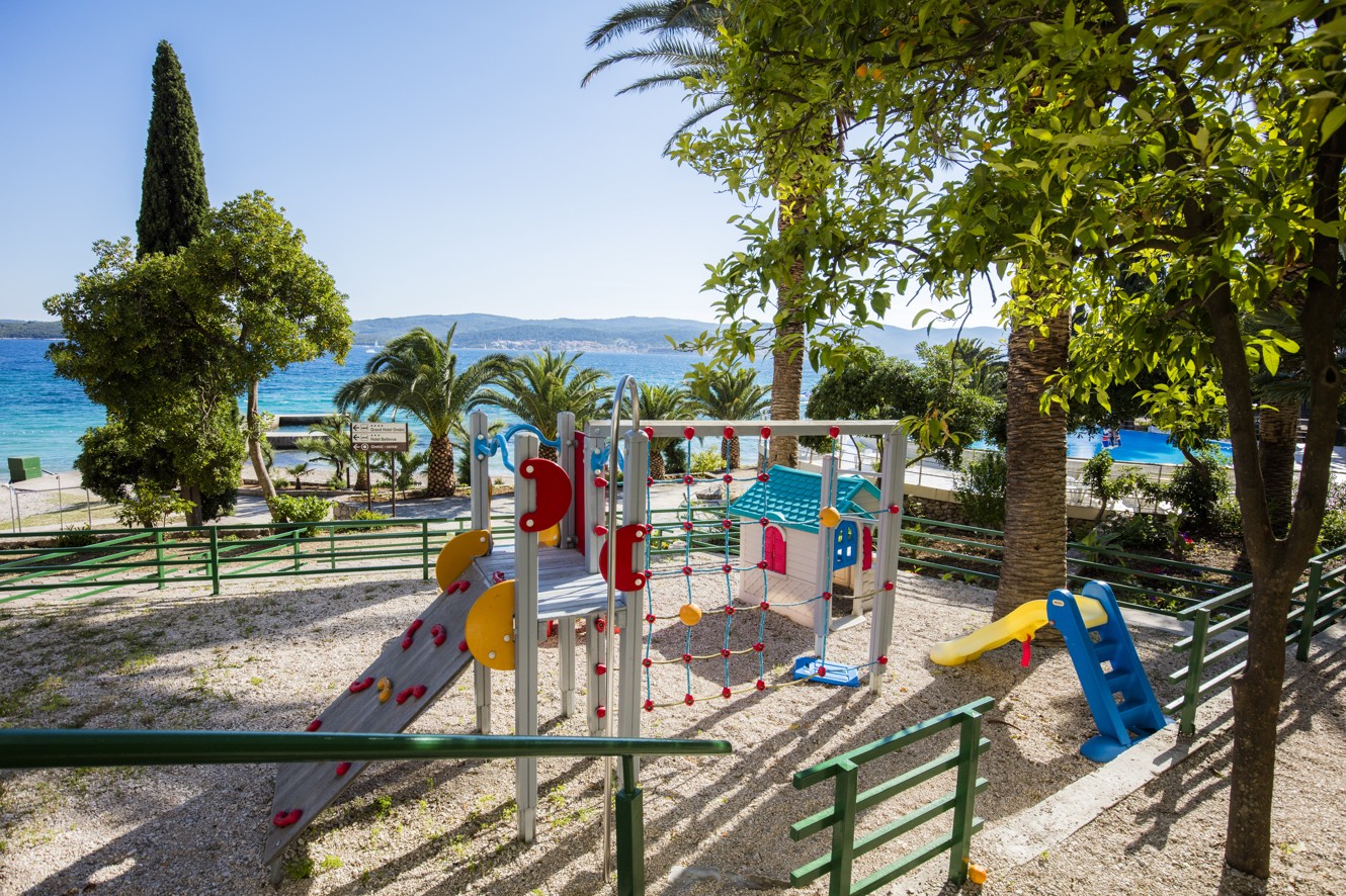 Buitenspeeltuin voor kinderen bij Maradiso Orsan by Aminess Hotel in Orebic met kleurrijke uitrusting, mediterrane bomen en uitzicht op zee.