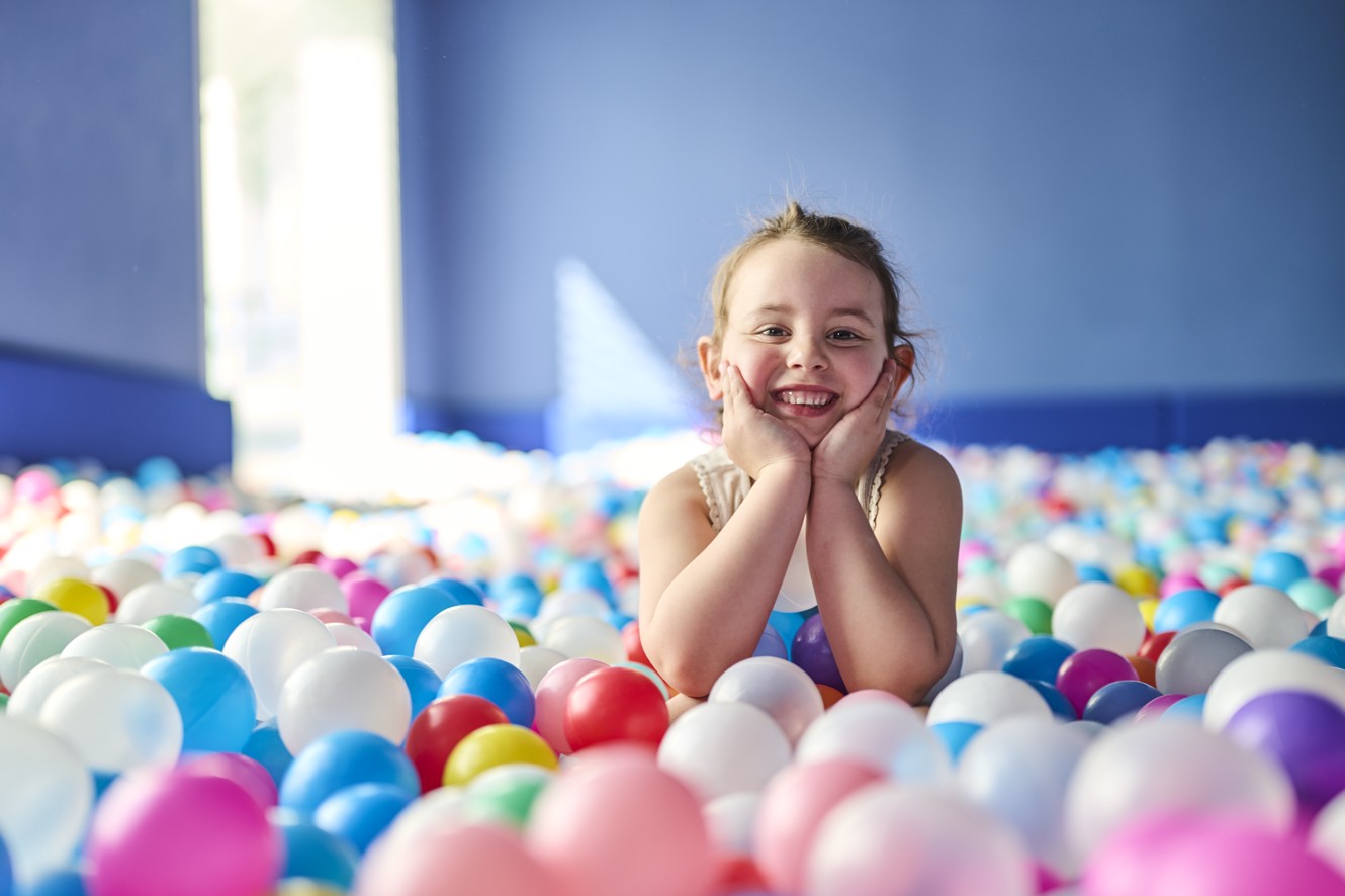 A smiling girl plays in a colorful ball pit in the kids playroom