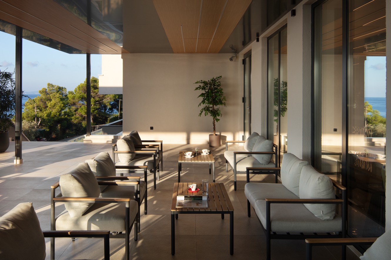 Overdekt loungeterras van de bar in het Aminess Alfir Resort met elegant meubilair, een ontspannen sfeer en uitzicht op zee en pijnbomen