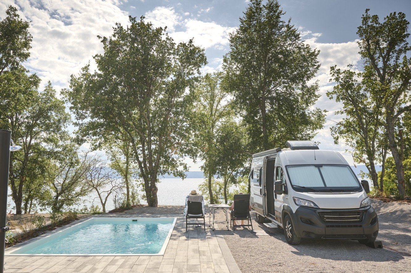 Območje bazena v Aminess Style Camping Atea Resort z ležalniki in bujnim drevesjem.