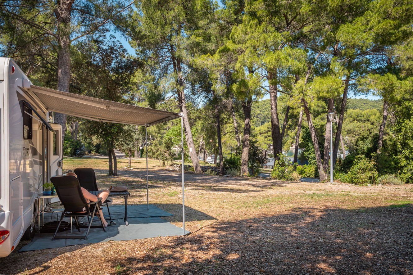 Comfortplaats bij Aminess Planet Camping Port9 Resort met caravan tussen de dennen.