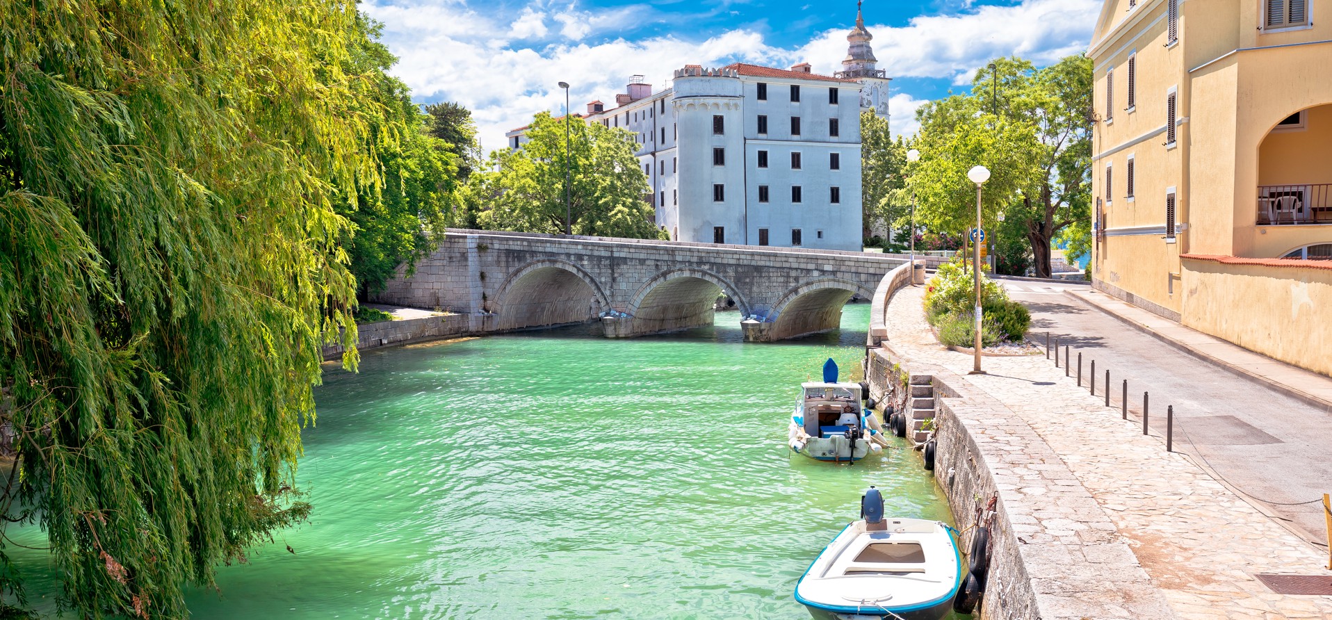 Vista panoramica dei resti del Monastero Pauline a Kaštel, Crikvenica, Croazia, con un ponte di pietra e barche lungo il fiume.