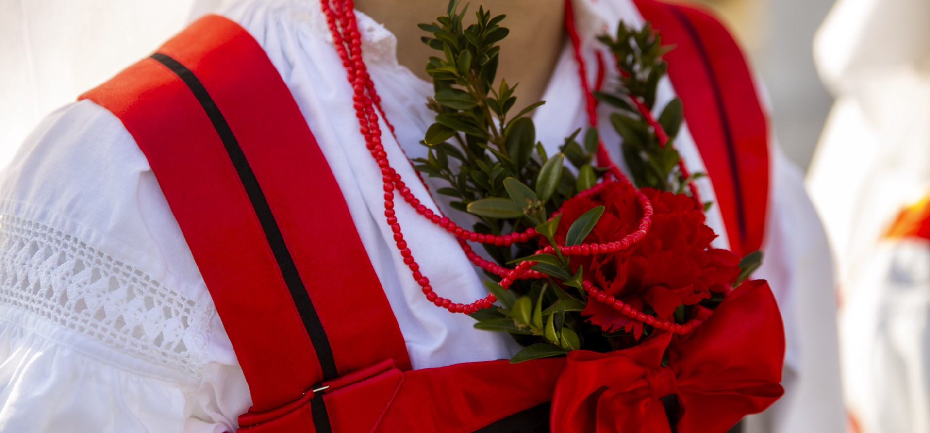 Traditional costume from Novi Vinodolski, Croatia, featuring red and white embroidery with decorative greenery.