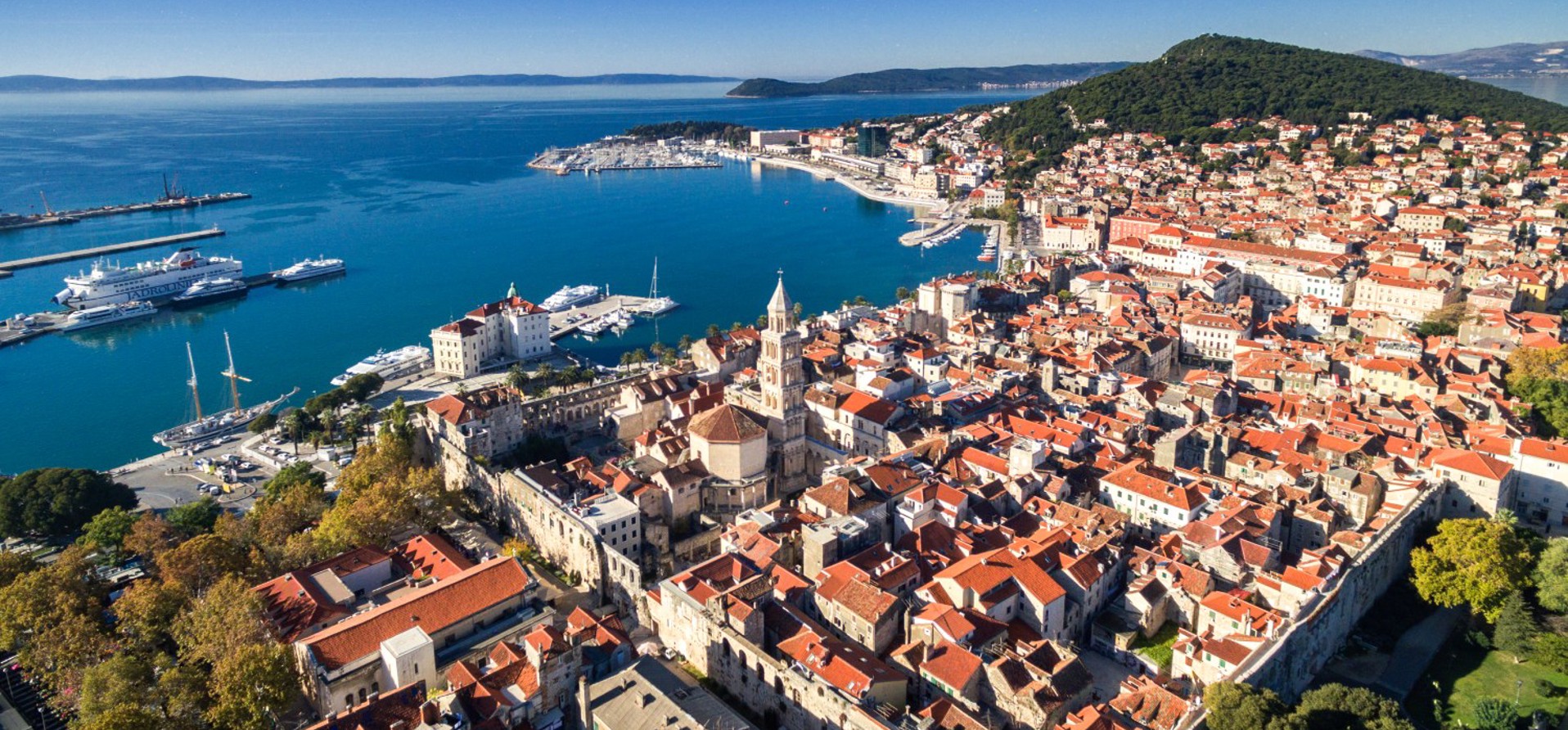 Scenic view of Split, Croatia, featuring historic architecture, a bustling waterfront, and the Adriatic Sea, as seen from Brač Island.