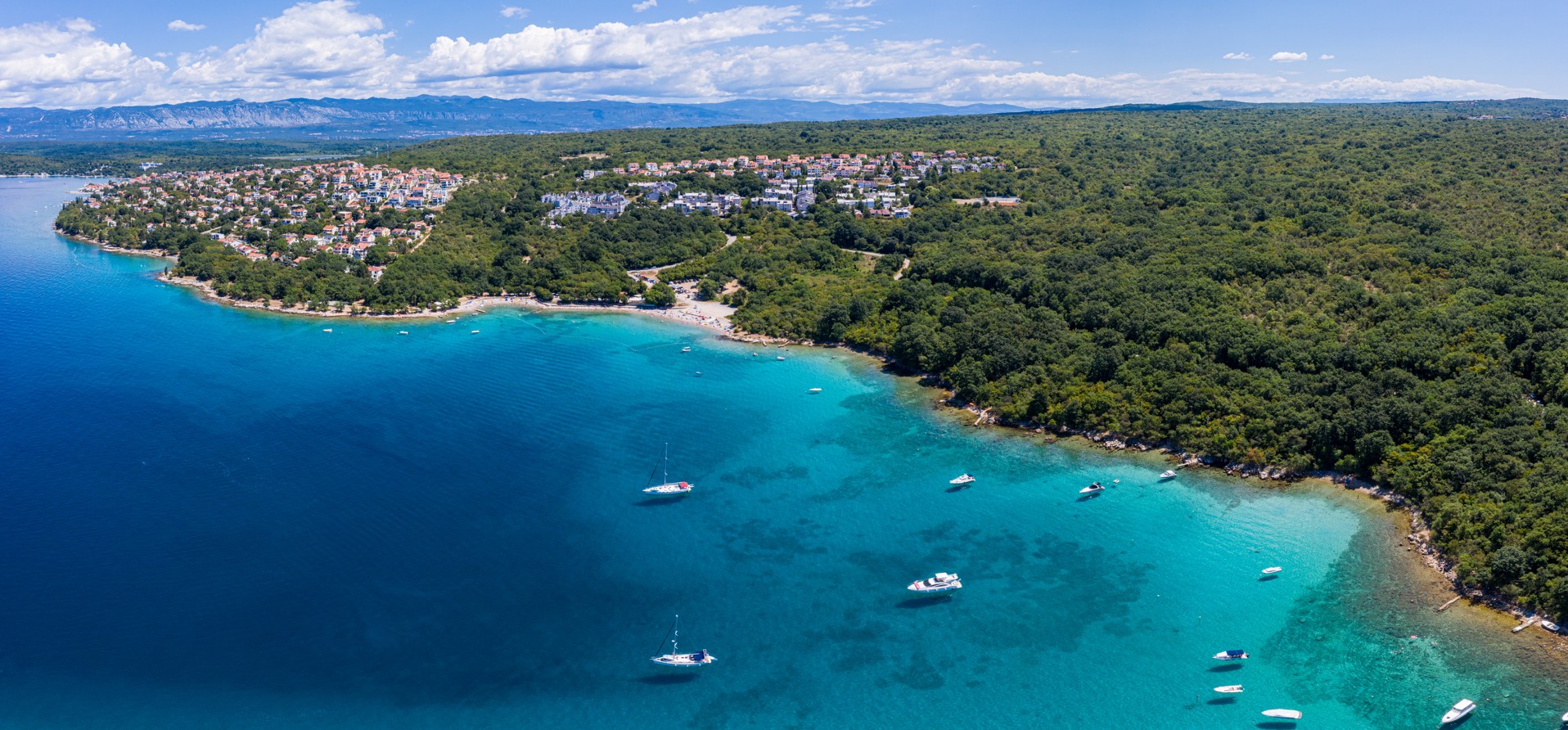 Aerial view of a beach with turquoise waters and boats along the coastline of Krk Island, Croatia.