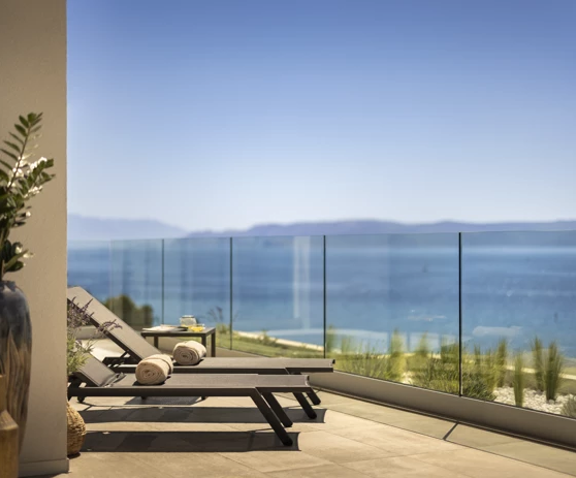 Mirna i elegantna terasa s ležaljkama i staklenom ogradom, koja pruža neometan pogled na more i udaljene planine.