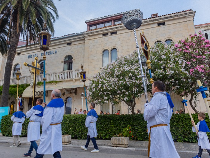 Participants in traditional attire take part in a cultural heritage procession near historic landmarks on Korcula Island.
