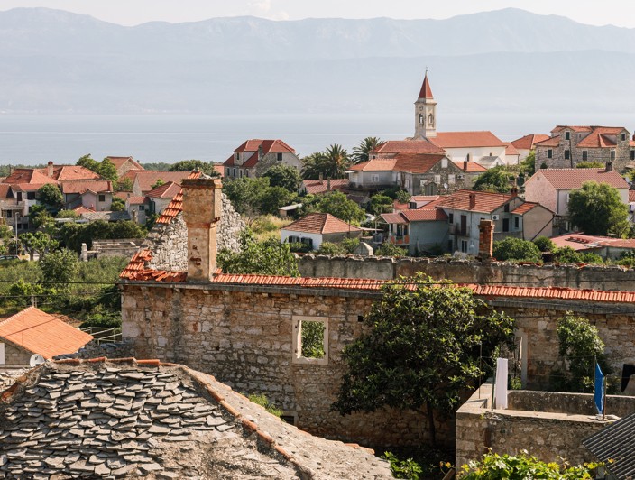 Traditionelles mediterranes Dorf auf der Insel Brač, Kroatien, mit Steinhäusern, engen Straßen und üppigem Grün.