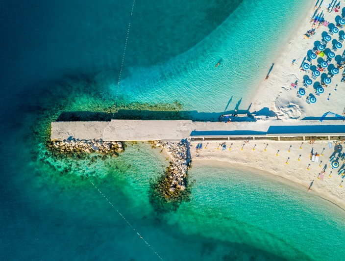 Aerial view of beach in Selce near Crikvenica, featuring turquoise sea and a pier surrounded by sunshades.
