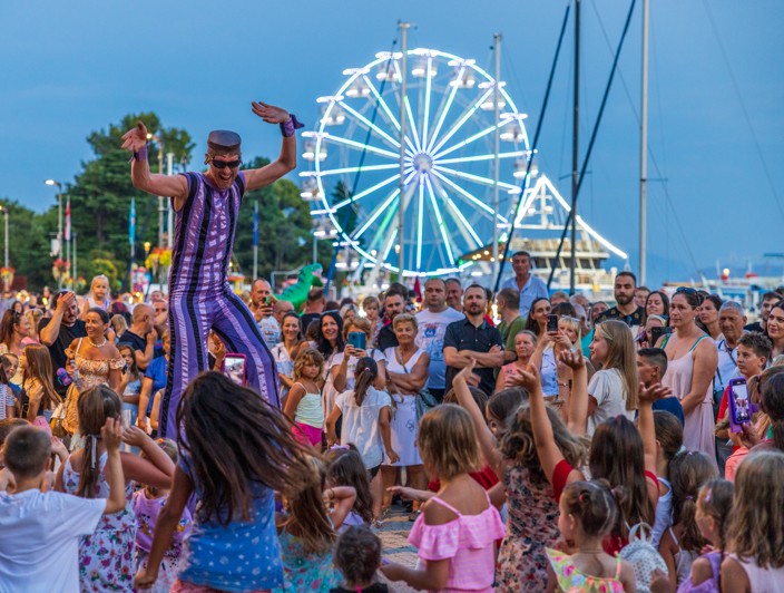 Evento CrikvArt a Crikvenica con una folla vivace, artisti e una ruota panoramica sullo sfondo.