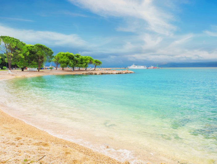 Sandy beach with clear sea and green trees along the coastline in Crikvenica, Croatia.