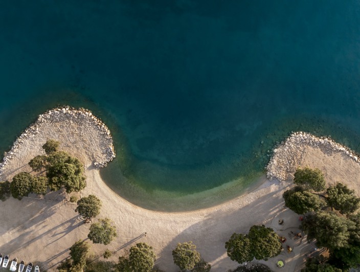 Aerial view of a beach with clear turquoise water and tree-lined shores in Crikvenica, Croatia.