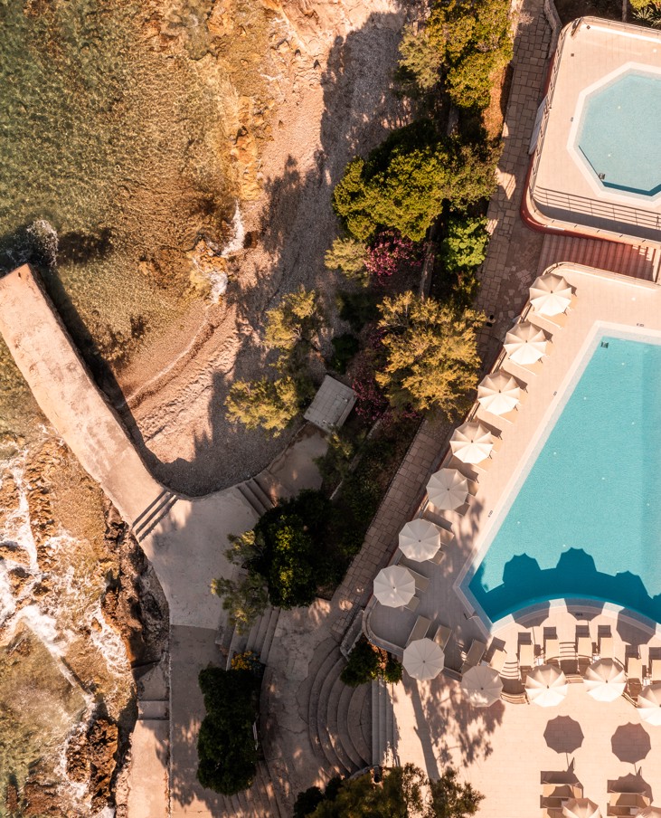 A bird's-eye view of the Aminess Younique Bellevue Hotel nestled amidst lush greenery, boasting a private beach and direct sea access.