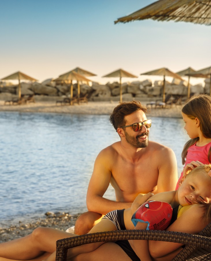 Famiglia che si rilassa sulla spiaggia al tramonto con lettini e mare.