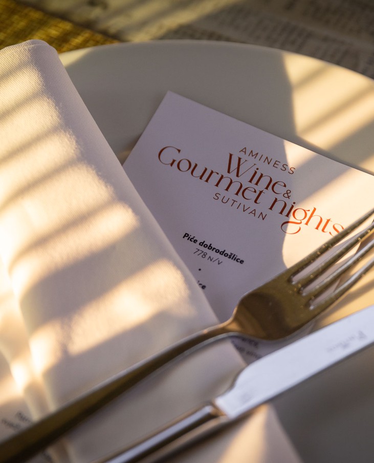 Menu gourmet con forchetta e coltello su piatto bianco in un ristorante a Sutivan alla luce della sera.