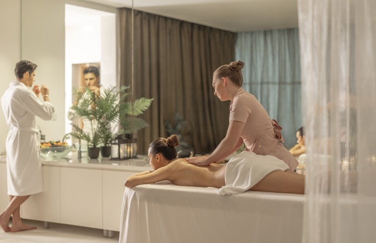 Coppia in una sala benessere per due in un resort, donna che riceve un massaggio mentre l'uomo si lava il viso.