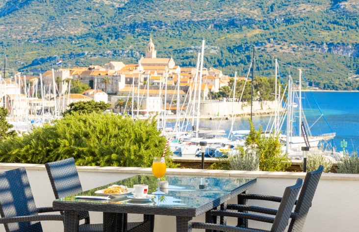 Bar uz bazen u Maradiso Marko Polo by Aminess u Korčuli s povišenim pogledom na marinu, zgrade grada s crvenim krovovima i bujno zelenilo.