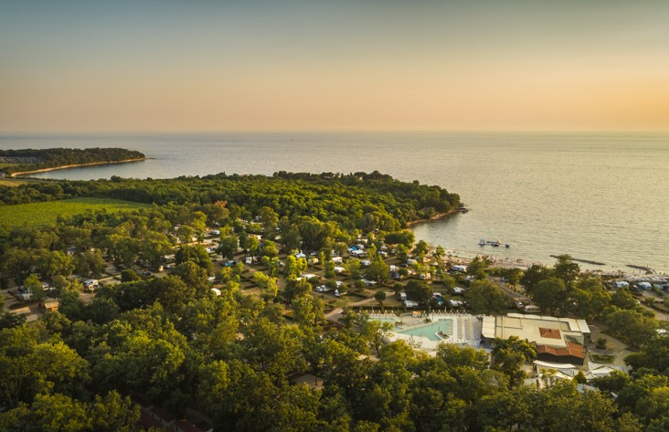 Luftaufnahme eines Campingplatzes am Meer mit Parzellen und viel Gruen in der Natur