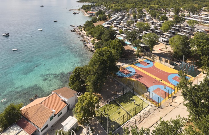View of the resort's new vibrant sports center, featuring courts surrounded by lush greenery and the tranquil Adriatic coastline at Aminess Style Camping Atea Resort.